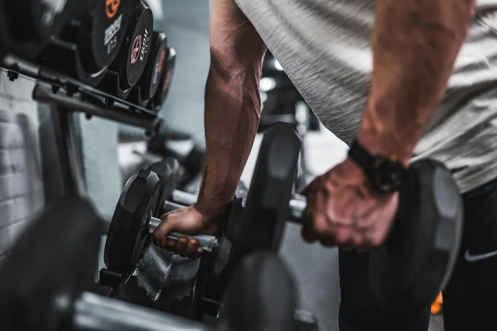 Pessoa escolhendo halteres em uma área de musculação